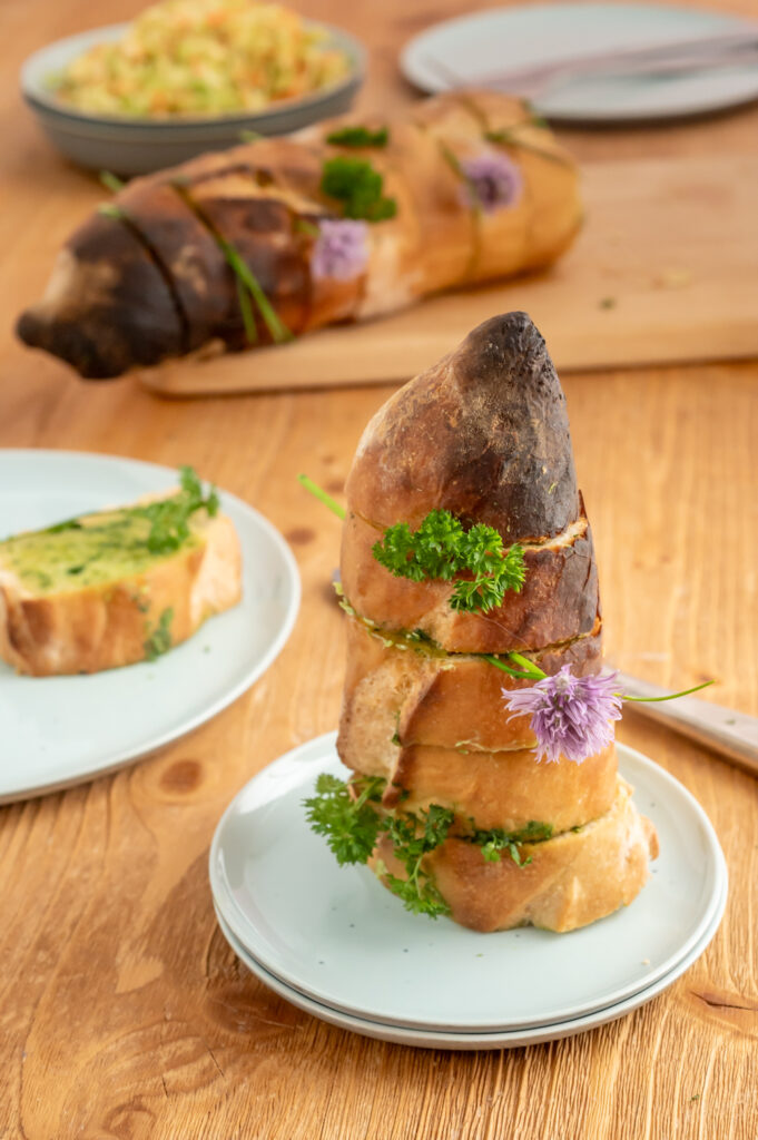 Schnell ein Kräuterbaguette selber machen. Einfach das Baguette einschneiden und mit Kräuterbutter füllen. Nach kurzer Zeit im Backofen, mit der restlichen Kräuterbutter füllen und mit frischen Kräutern dekorieren. 