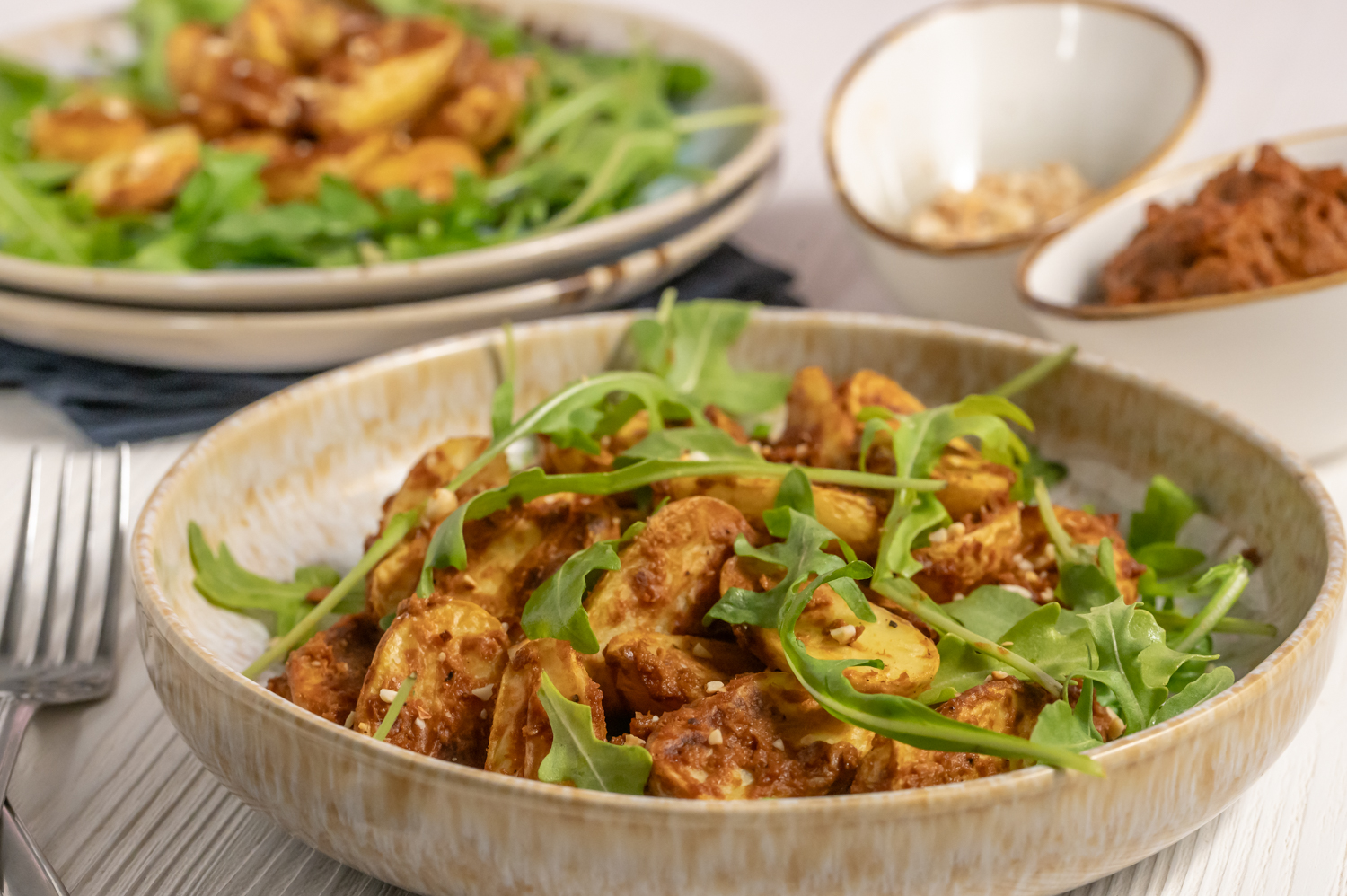 Ein einfaches Rezept für Kartoffelsalat mit Pesto aus Ofenkartoffeln und rotem Pesto. Serviert mit frischem Rucola und gerösteten Cashewkernen.
